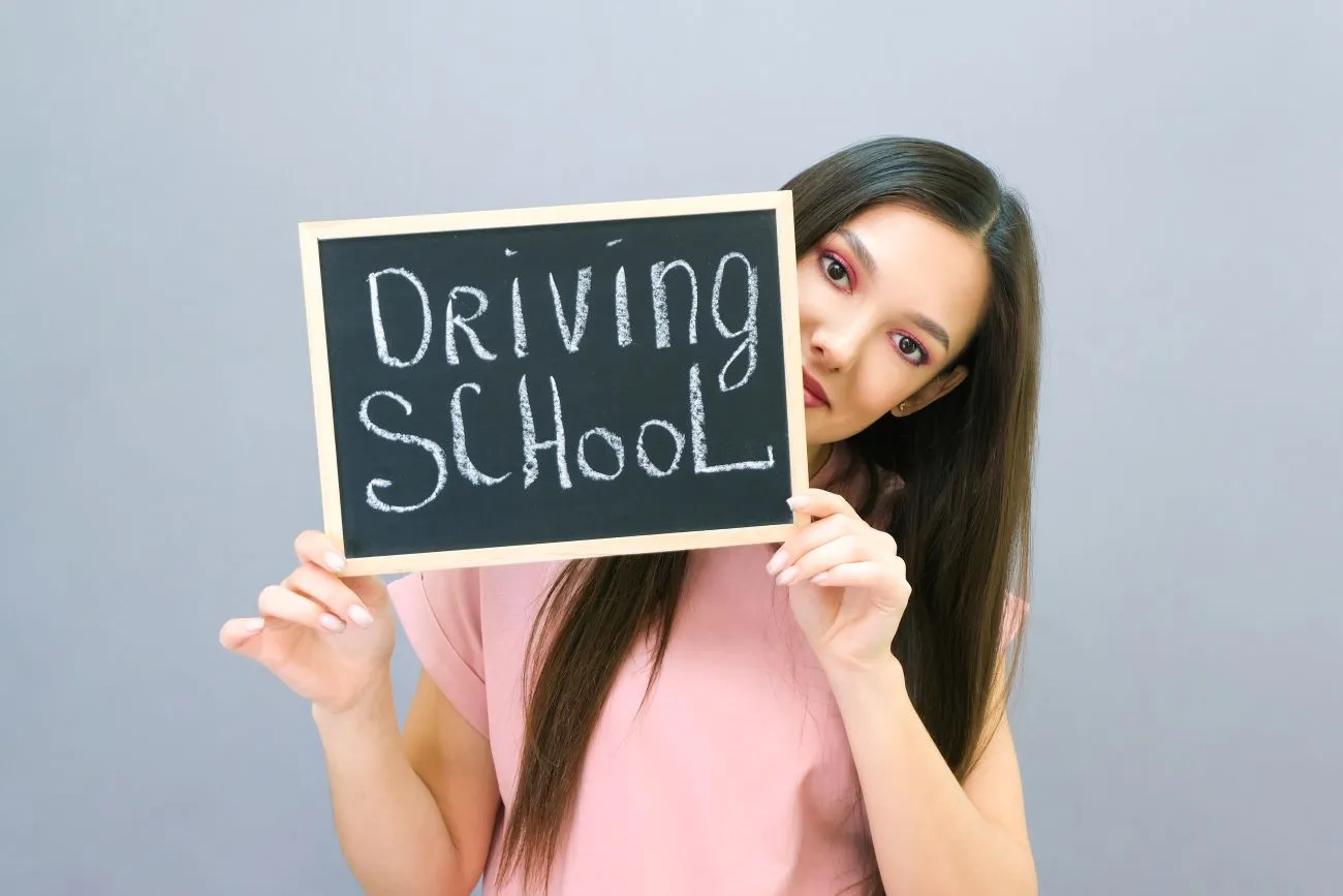 Young woman holding driving lessons school sign